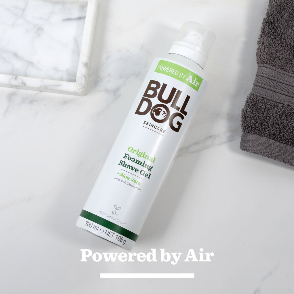 A can of Original Foaming Shave Gel with natural origin ingredients sits on a light surface beside a gray towel and marble tray. The phrase Powered by Air appears at the bottom.