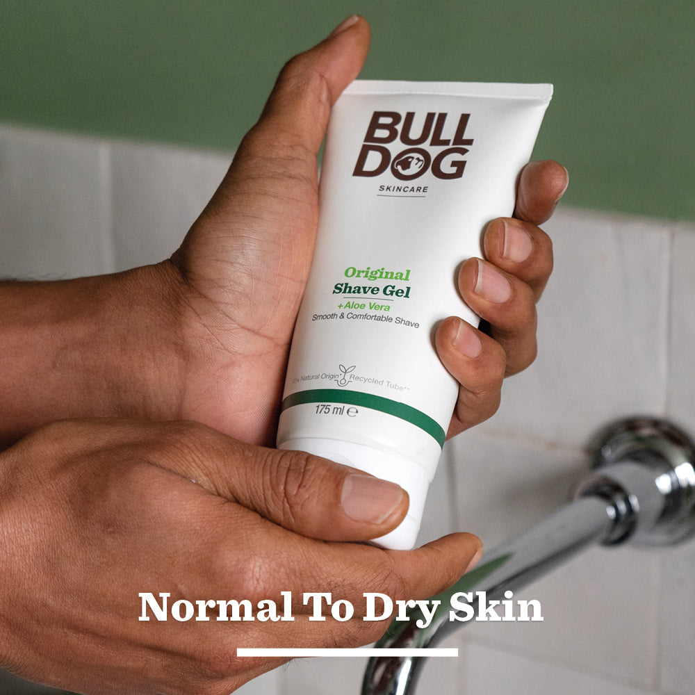 A person holds a tube of Original Shave Gel for men with aloe vera and natural origin ingredients near a sink. White text at the bottom reads, Normal To Dry Skin.