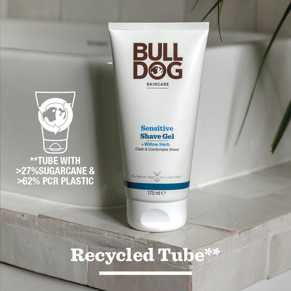 A tube of Sensitive Shave Gel for men rests on a bathroom counter, featuring natural origin ingredients. The packaging contains 27%+ sugarcane, 62% recycled plastic, and displays “Recycled Tube” at the bottom.