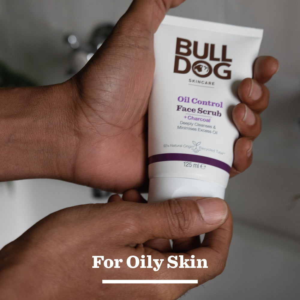 A person holds a tube of Oil Control Face Scrub, designed for oily skin, featuring natural origin ingredients that deeply cleanse and help control excess oil.