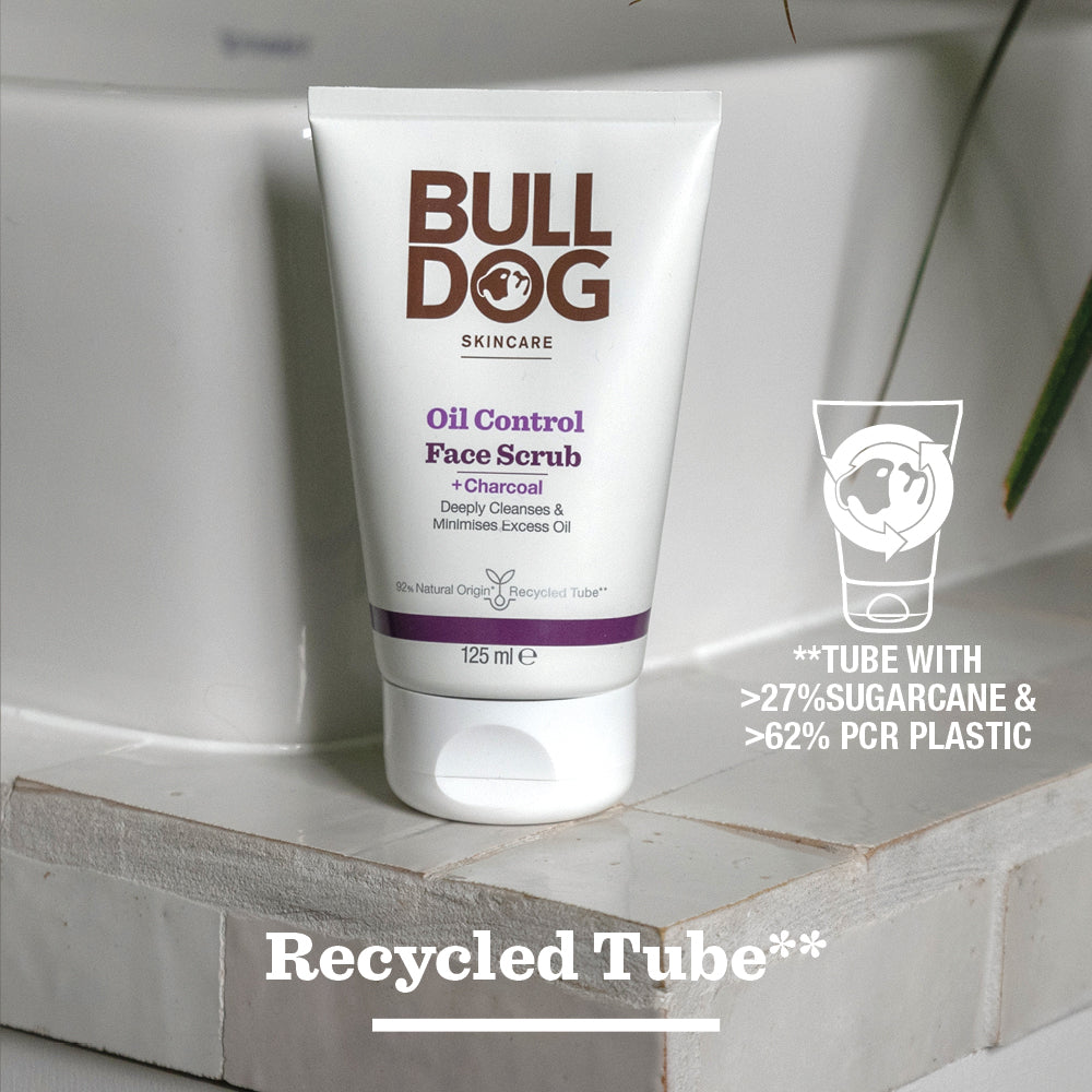 A tube of Oil Control Face Scrub rests on wood, highlighting its charcoal and natural origin ingredients. The packaging contains 27% sugarcane and 62% recycled plastic.