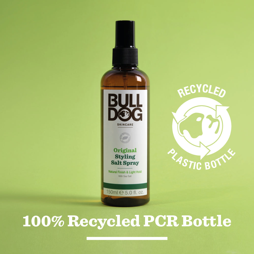 A bottle of Original Hair Styling Salt Spray stands on a green background, made with Mediterranean sea salt and naturally derived ingredients. The 100% recycled PCR plastic bottle displays a recycling symbol and Recycled Plastic Bottle text.