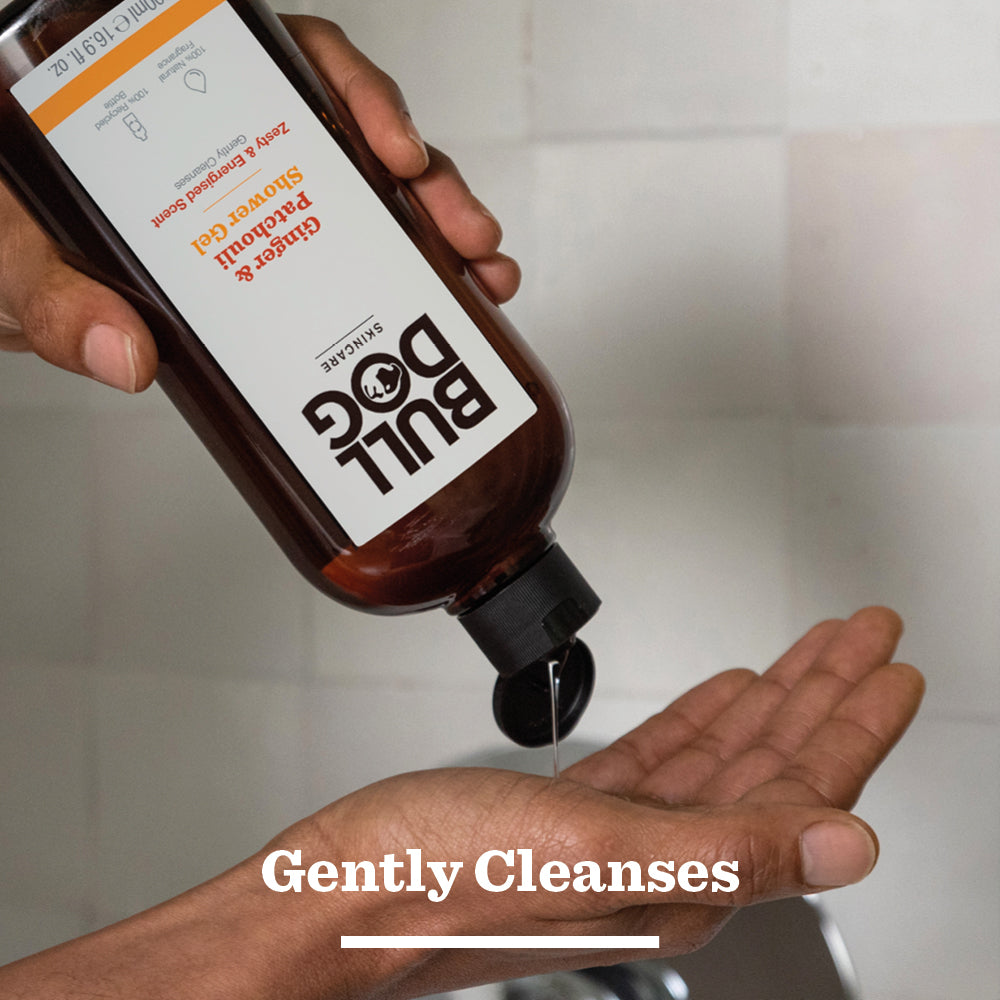 A person pours Ginger & Patchouli Shower Gel from a brown bottle into their palm over a sink. Text at the bottom reads “Gently Cleanses.”.