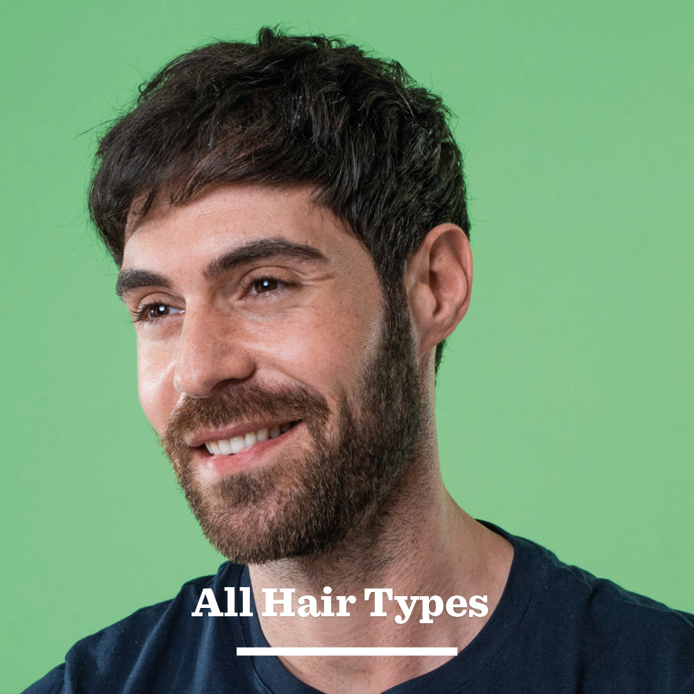 A smiling man with short brown hair and a beard poses in front of a green background, wearing a dark shirt. Text at the bottom reads All Hair Types. Ideal for showcasing Original Hair Styling Clay, which delivers a natural, matte finish.