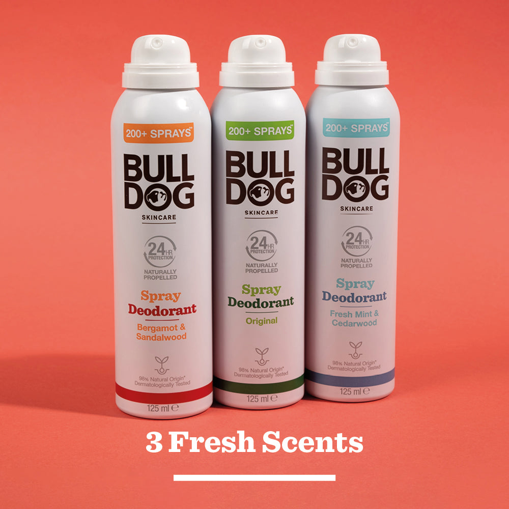 Three Bulldog spray deodorant cans—Bergamot & Sandalwood, Original, and Fresh Mint & Cedarwood—stand side by side on a red background; each is vegan and made with natural ingredients for fresh scent options.