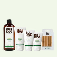 The Original Dry Skin Regime Bundle features vegan Bulldog Skincare products—shower gel, face wash, face scrub, and aloe vera moisturizer for dry skin—plus a bamboo soap dish, all displayed side by side against a light background.